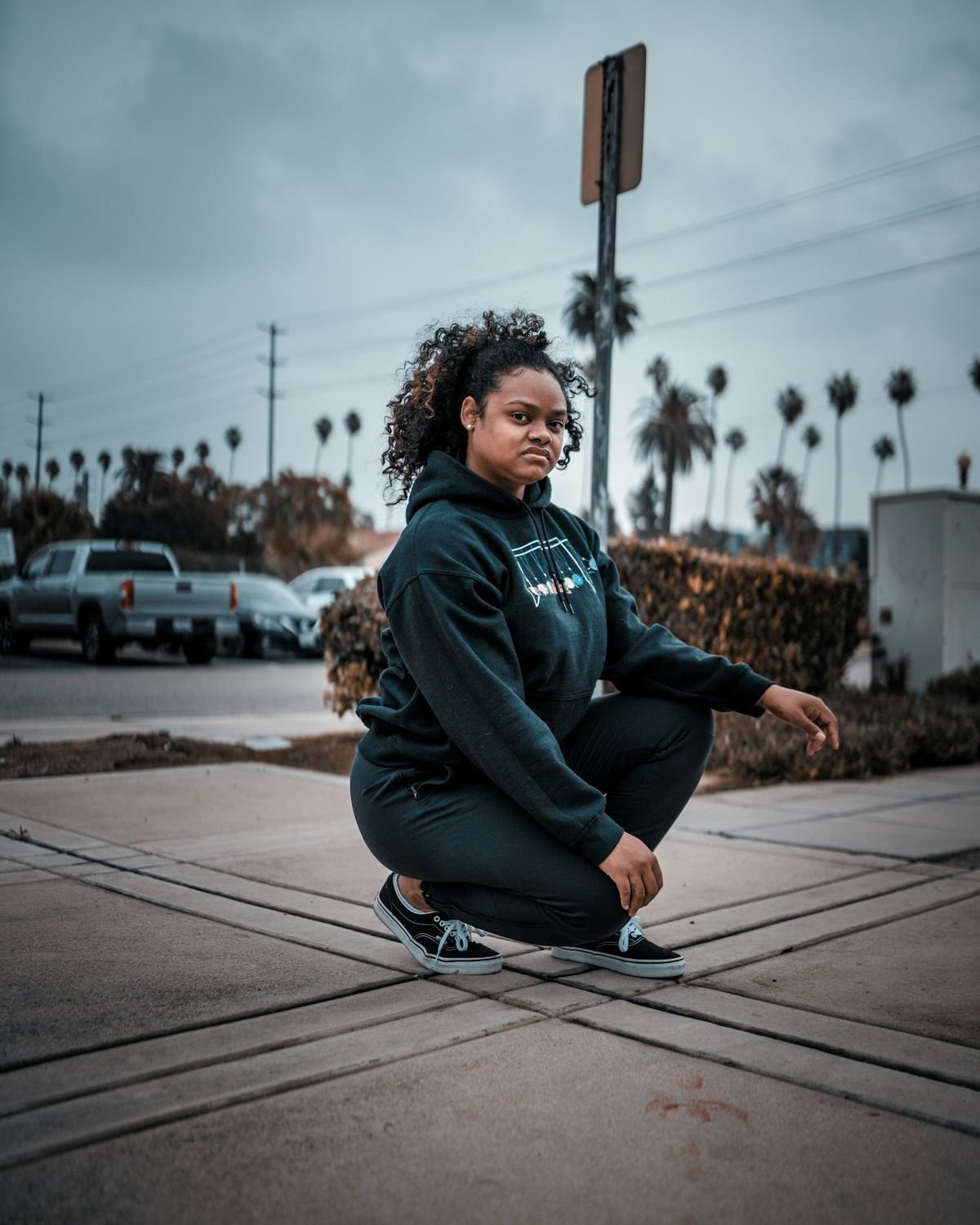 Woman in a black hoodie on a palm-lined city street